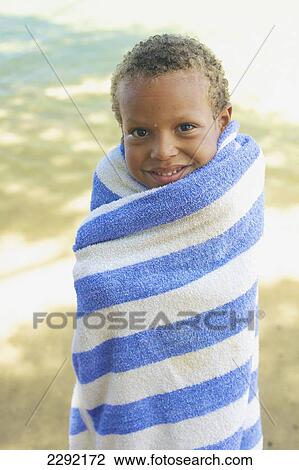 Stock Image - A young boy wrapped up in a towel on the beach; Hawaii united states of america. Fotosearch