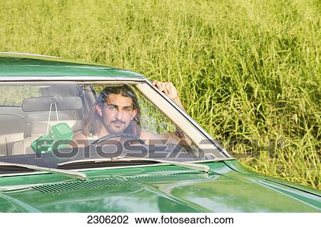 Stock Image - A young man drives a green vintage car with green fuzzy dice hanging from the rearview mirror; Hawaii united states of america. Fotosearch