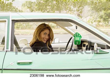 Stock Photo - A young woman sits in a vintage green car with green fuzzy dice hanging from the rearview mirror; Hawaii united states of america. Fotosearch