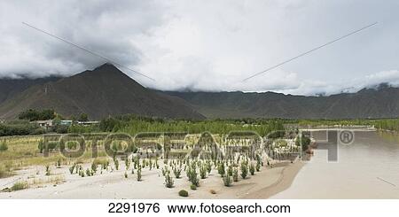 Stock Photograph - Landscape of a mountain range and a river under a cloudy sky; Lhasa xizang china. Fotosearch