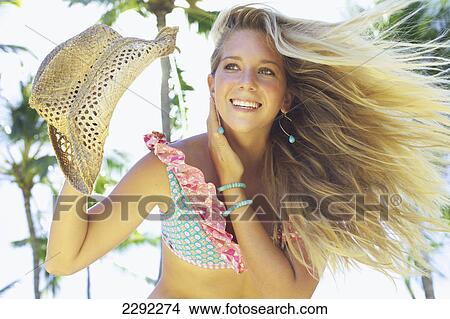 Picture - Portrait of a teenage girl in a bikini with windblown hair holding a hat; Maui hawaii united states of america. Fotosearch