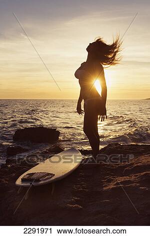 Silhouette of a woman standing on a rock at the water's edge with her surfboard at sunset; Tarifa cadiz andalusia spain View Large Photo Image Stock Image - Silhouette of a woman standing on a rock at the water's edge with her surfboard at sunset; Tarifa cadiz andalusia spain. Fotosearch