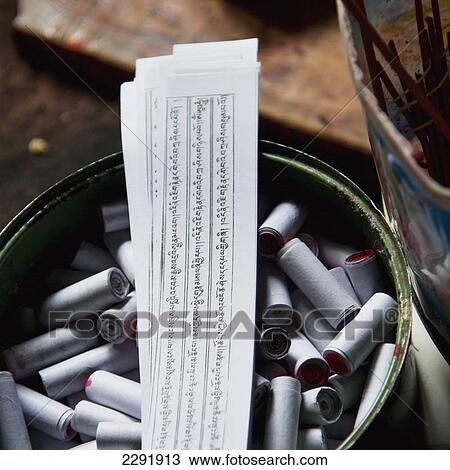 Stock Image - Strips of paper in a pile resting on rolled papers in a container; Lhasa xizang china. Fotosearch
