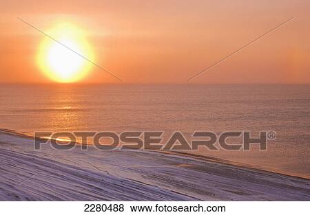 The setting sun shining through windblown snow creates a sundog above the beaufort sea along the coast just outside of barrow in winter; Alaska united states of america View Large Photo Image Stock Photo - The setting sun shining through windblown snow creates a sundog above the beaufort sea along the coast just outside of barrow in winter; Alaska united states of america. Fotosearch