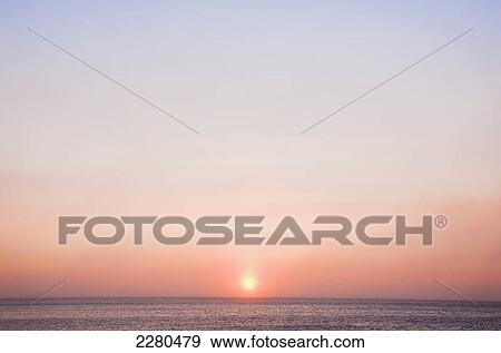 Stock Photo - The sun shines through windblown snow above the beaufort sea coast just before it sets outside of barrow in winter; Alaska united states of america. Fotosearch