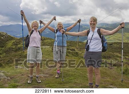 Stock Image - Three women with trekking poles raise arms in the air in celebration of accomplishment; Gowbarrow fell ullswater lake district cumbria england. Fotosearch