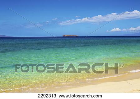 Stock Image - View of a rock formation and coastline of an hawaiian island in the distance from the sandy shore; Hawaii united states of america. Fotosearch