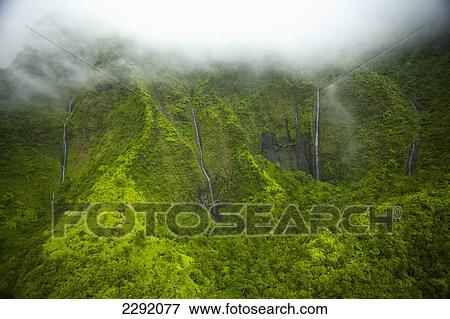 Stock Photo - Waterfalls flowing through lush green hills under the low lying clouds; Hawaii united states of america. Fotosearch