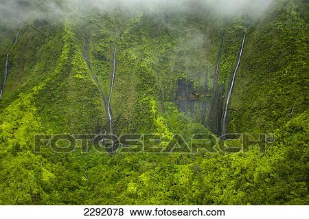 Stock Photo - Waterfalls flowing through lush green hills under the low lying clouds; Hawaii united states of america. Fotosearch