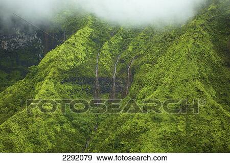 Stock Photo - Waterfalls flowing through lush green hills under the low lying clouds; Hawaii united states of america. Fotosearch