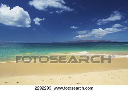 Stock Image - Waves of the pacific ocean rolling onto a white sand beach of an hawaiian island with mountains in the distance; Hawaii united states of america. Fotosearch