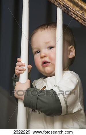 A baby boy holds on to the stair rail balusters with both hands; Willimantic connecticut united states of america View Large Photo Image Stock Photo - A baby boy holds on to the stair rail balusters with both hands; Willimantic connecticut united states of america. Fotosearch