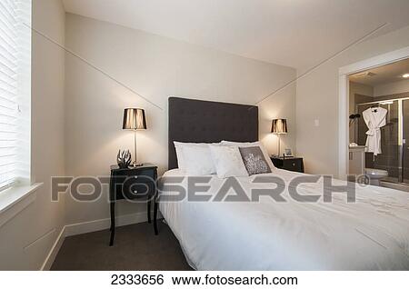 Stock Photograph - A bed in a bedroom with an attached bathroom; Surrey, British Columbia, Canada. Fotosearch