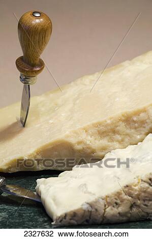 Stock Image - A block of parmesan and gorgonzola cheese on a marble round board with knives; Calgary alberta canada. Fotosearch