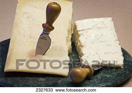 Stock Image - A block of parmesan and gorgonzola cheese on a marble round board with knives; Calgary alberta canada. Fotosearch