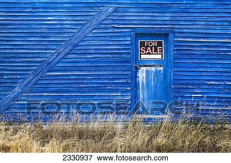 Stock Photo - A blue barn with a for sale sign in the window of the door; Saskatchewan canada. Fotosearch
