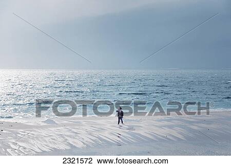 Stock Image - A Businessman Using A Cell Phone Stands At The Water's Edge In The Tide; Tarifa Cadiz Andalusia Spain. Fotosearch