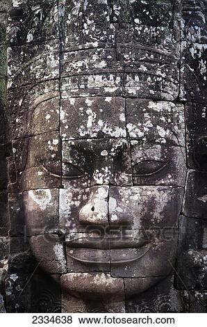 Stock Photo - A face sculpture on a stone wall at Angkor Wat; Cambodia. Fotosearch
