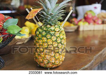 Stock Image - A fresh pineapple with straws and a paper umbrella sitting on a counter; Hawaii united states of america. Fotosearch