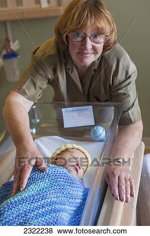 Stock Photo - A grandmother admires her first grandchild in a hospital bassinet; Willimantic connecticut united states of america. Fotosearch