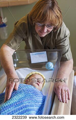 A grandmother admires her first grandchild in a hospital bassinet; Willimantic connecticut united states of america View Large Photo Image Stock Photo - A grandmother admires her first grandchild in a hospital bassinet; Willimantic connecticut united states of america. Fotosearch