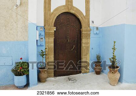 Stock Photograph - A House With An Arched Wooden Door With Rivets And Painted Blue Walls In Old Town; Rabat Morocco. Fotosearch