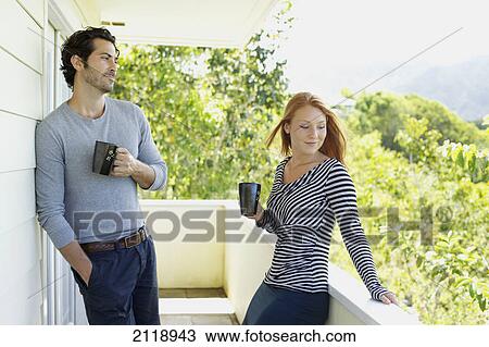 Stock Image - A Man And Woman Standing On A Balcony With Their Coffee Mugs; Wailua Kauai Hawaii United States Of America. Fotosearch