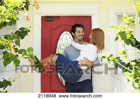 Stock Photo - A Man Carries A Woman Over The Threshold At The Front Door; Wailua Kauai Hawaii United States Of America. Fotosearch