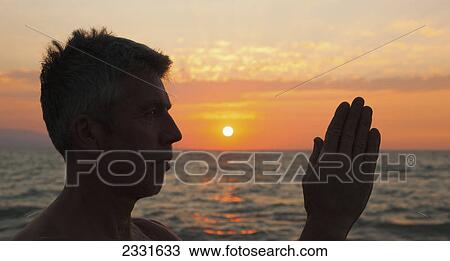 Stock Image - A man in prayer or yoga pose as the sun set on a tropical beach; Puerto vallarta mexico. Fotosearch