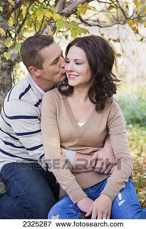 A man kissing a woman on the cheek in a park in autumn; St. albert alberta canada View Large Photo Image Stock Photo - A man kissing a woman on the cheek in a park in autumn; St. albert alberta canada. Fotosearch