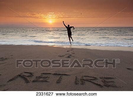 Stock Photo - A man leaps for joy on a tropical beach with the word retire written in the sand; Puerto vallarta mexico. Fotosearch