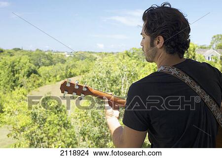 Picture - A Man Playing His Guitar With A View Of The Lush Landscape; Wailua Kauai Hawaii United States Of America. Fotosearch