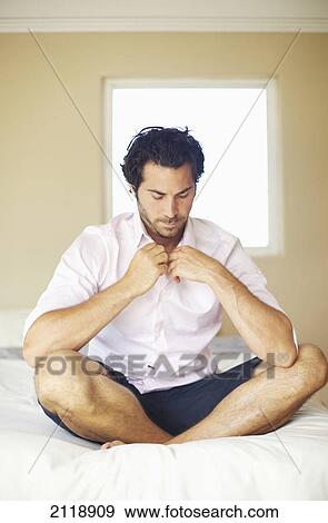 A Man Sitting Crossed-Legged On A Bed Buttoning Up His Shirt; Wailua Kauai Hawaii United States Of America View Large Photo Image Stock Photo - A Man Sitting Crossed-Legged On A Bed Buttoning Up His Shirt; Wailua Kauai Hawaii United States Of America. Fotosearch