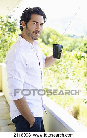 Stock Image - A Man Standing On A Balcony Drinking A Cup Of Coffee; Wailua Kauai Hawaii United States Of America. Fotosearch