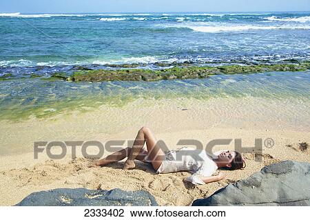 Stock Image - A model lays out on the beach; Kauai hawaii united states of america. Fotosearch