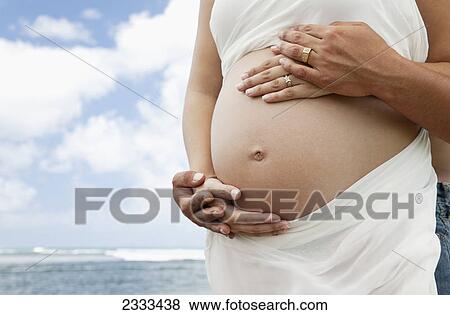 A pregnant woman and her husband with hands on her bare belly at the ocean; Honolulu hawaii united states of america View Large Photo Image Stock Photo - A pregnant woman and her husband with hands on her bare belly at the ocean; Honolulu hawaii united states of america. Fotosearch