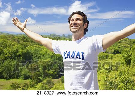 Stock Photo - A Smiling Man Stands With Arms Raised And Lush Vegetation In The Background; Wailua Kauai Hawaii United States Of America. Fotosearch
