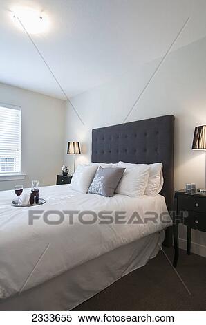 Stock Photography - A tray with a flask and two glasses of red wine on a bed in a bedroom; Surrey, British Columbia, Canada. Fotosearch