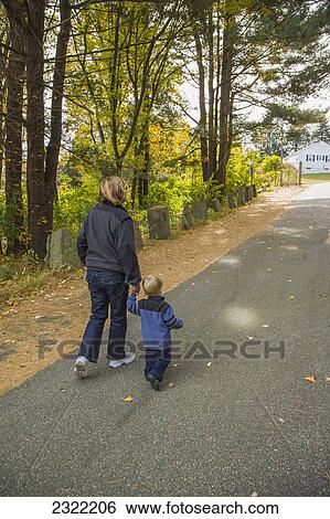 Stock Photograph - A two-year old boy walks on a paved road in a park holding his grandmother's hand; Willimantic connecticut united states of america. Fotosearch