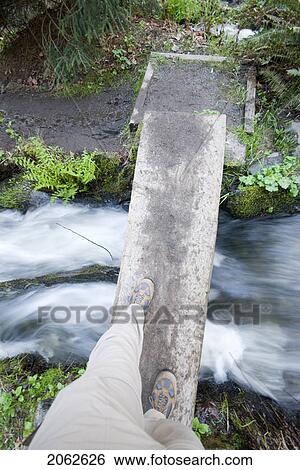 Stock Photograph - A View Of A Hikers Feet As He Walks Across A Narrow Bridge Over A Rushing Creek, Royal Roads University Campus Near Victoria, Bc, Canada. Fotosearch