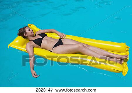Stock Photo - A woman lounging on a yellow inflatable mattress in a swimming pool; Cyprus. Fotosearch