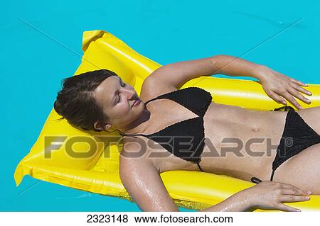 Stock Photo - A woman lounging on a yellow inflatable mattress in a swimming pool; Cyprus. Fotosearch