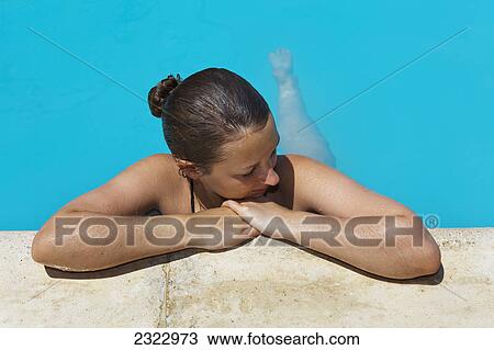 Stock Image - A woman relaxing at the edge of a swimming pool; Cyprus. Fotosearch
