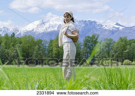 A woman stands in a grass field with the alps mountain range in the background; Locarno ticino switzerland View Large Photo Image Picture - A woman stands in a grass field with the alps mountain range in the background; Locarno ticino switzerland. Fotosearch