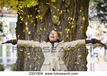 A woman stands in front of a tree with arms outstretched as yellow leaves shower down on her; Locarno ticino switzerland View Large Photo Image Picture - A woman stands in front of a tree with arms outstretched as yellow leaves shower down on her; Locarno ticino switzerland. Fotosearch