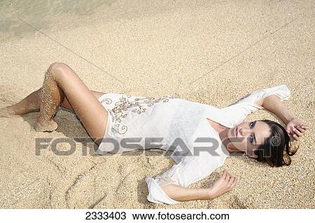 Stock Image - A young woman modelling and laying on the beach; Kauai hawaii united states of america. Fotosearch