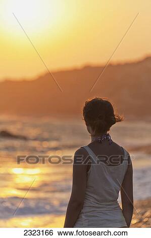 A young woman stands at the water's edge watching the sunset; Aphrodite bay cyprus View Large Photo Image Stock Photograph - A young woman stands at the water's edge watching the sunset; Aphrodite bay cyprus. Fotosearch