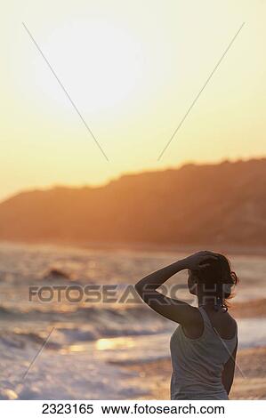 A young woman stands at the water's edge watching the sunset; Aphrodite bay cyprus View Large Photo Image Stock Photography - A young woman stands at the water's edge watching the sunset; Aphrodite bay cyprus. Fotosearch
