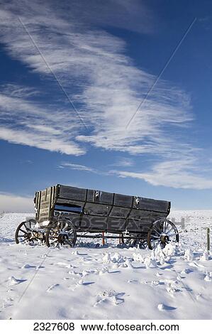 Stock Photo - An old wooden wagon on a snow covered hillside with blue sky and clouds; Alberta canada. Fotosearch