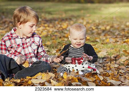Baby girl and her brother playing in the fallen leaves in a park in autumn; Edmonton alberta canada View Large Photo Image Picture - Baby girl and her brother playing in the fallen leaves in a park in autumn; Edmonton alberta canada. Fotosearch